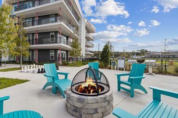 A fire pit sits in the middle of a patio with blue chairs and benches around it